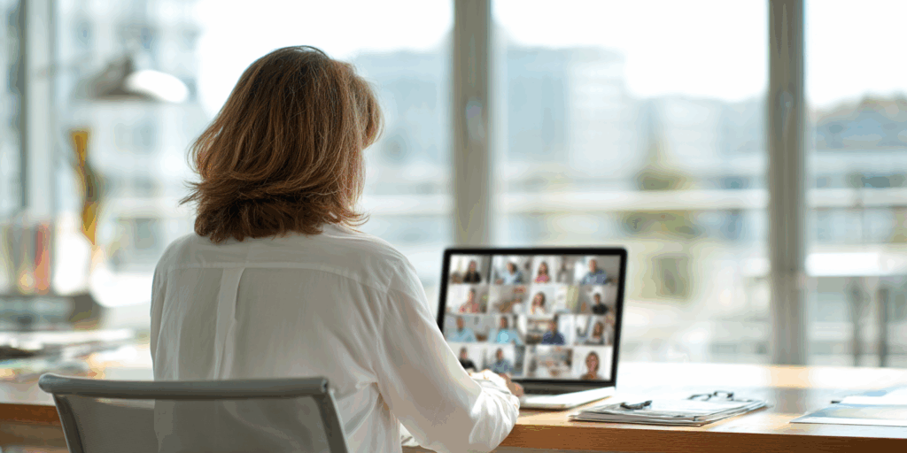 Eine Frau sitzt an einem Schreibtisch und schaut auf einen Bildschirm, auf dem viele Fotos von Personen zu sehen sind.